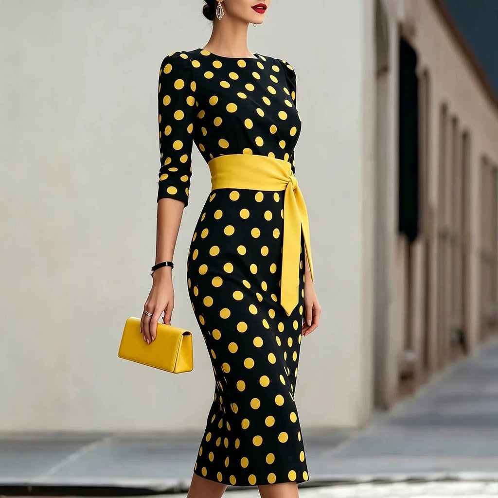 Woman wearing a black dress with yellow polka dots and a matching belt, holding a yellow clutch.