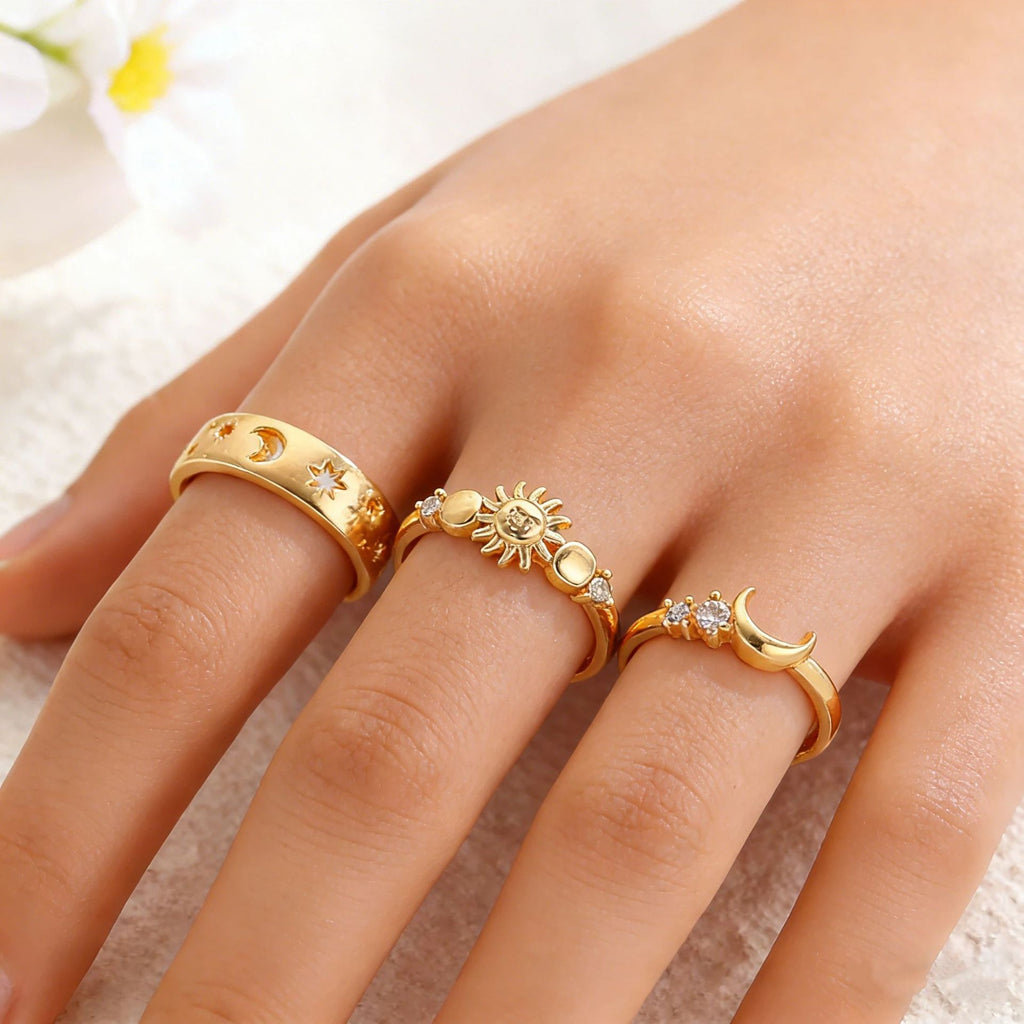 Gold rings with sun, moon, and star designs on a hand against a soft background