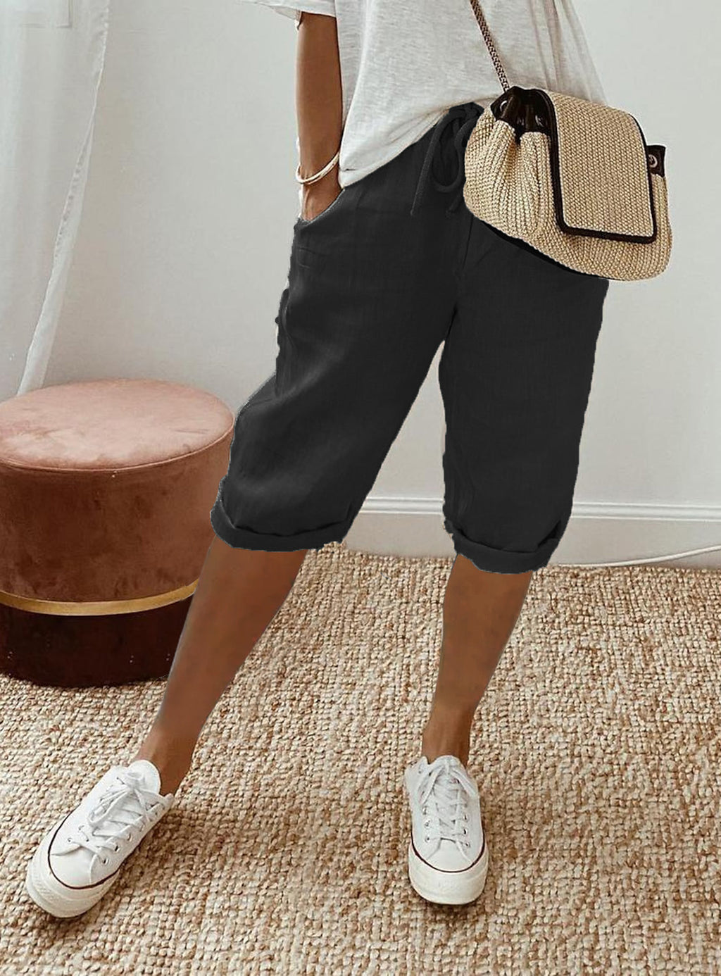 Person wearing black shorts, white sneakers, and a straw bag indoors.