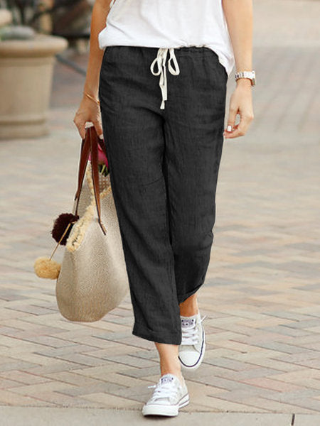 Person wearing black pants with a drawstring, white shirt, and sneakers on a paved walkway.