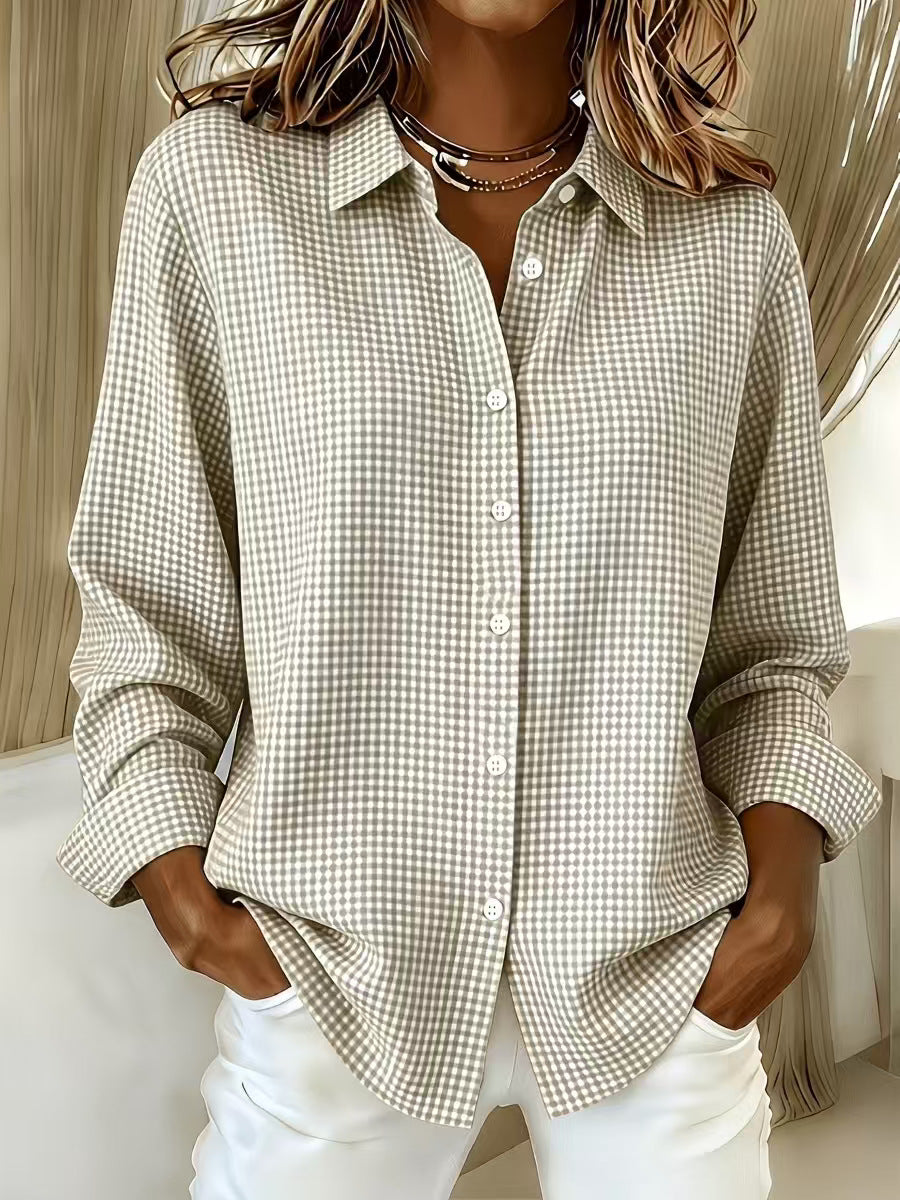 A woman wearing a beige and white gingham check long-sleeve button-up shirt with white pants, standing in an indoor setting.