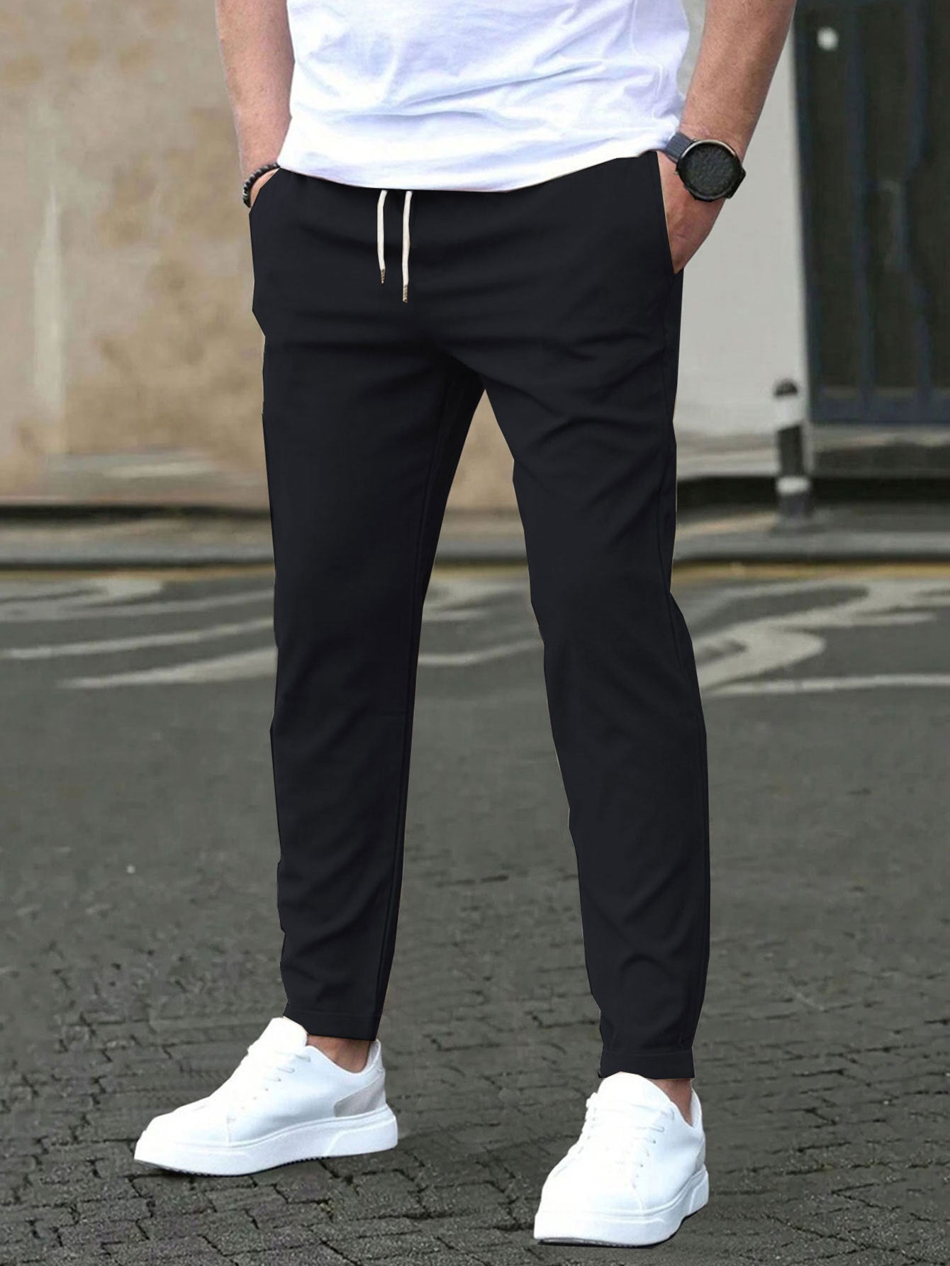 Person wearing black jogger pants, white shirt, and white sneakers on a street.