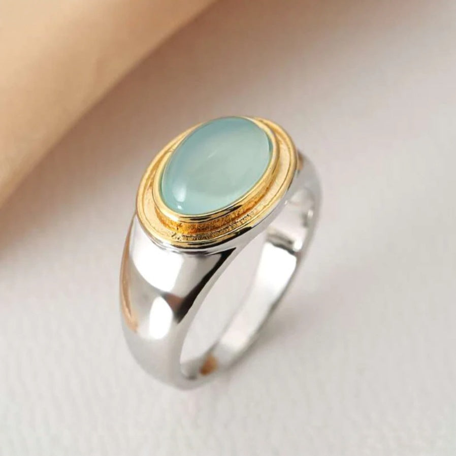 Ring with a gold and silver band and a green stone on a beige background