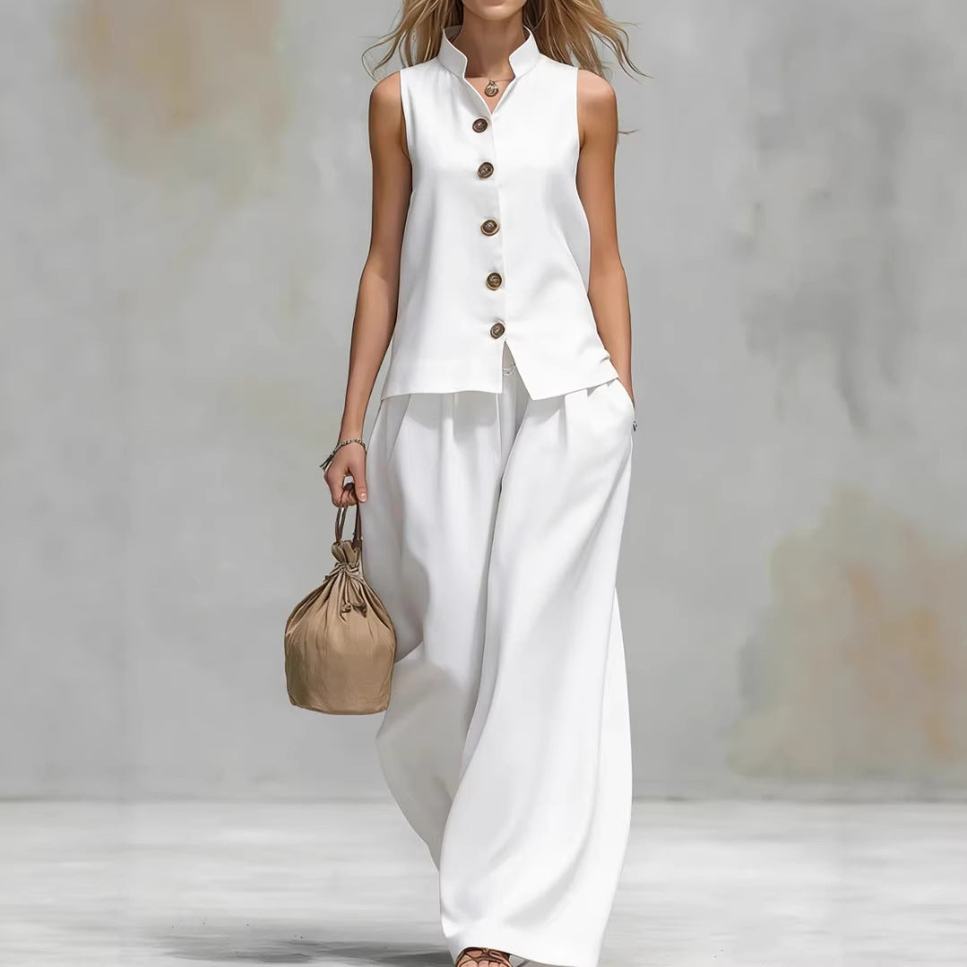 Woman wearing a white sleeveless top and pants with a beige handbag on a light gray background