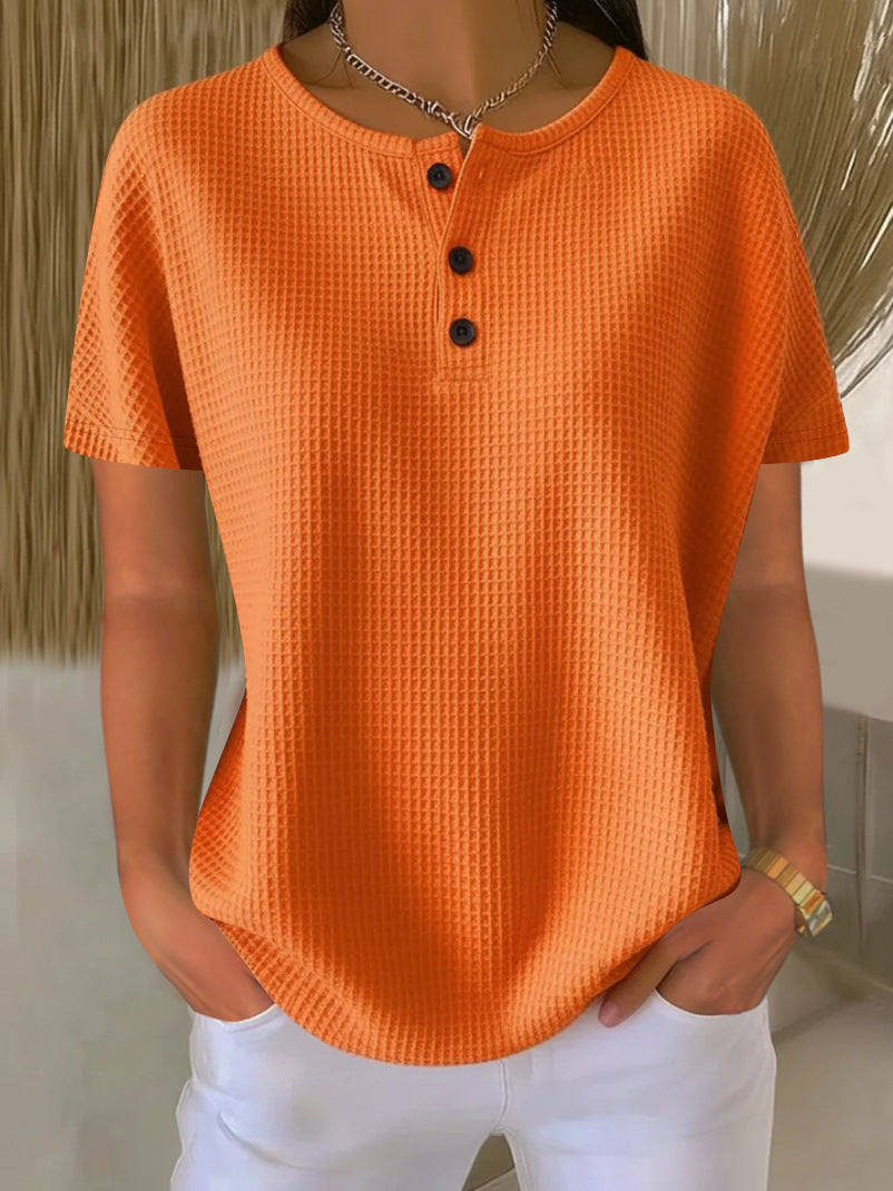 Person wearing an orange textured shirt with black buttons against a neutral background