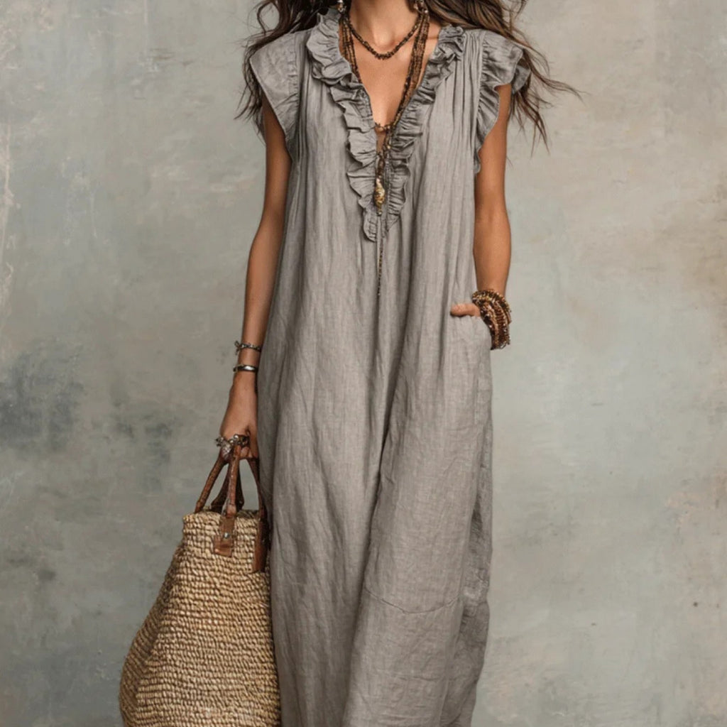 Woman wearing a gray ruffled dress holding a straw bag against a textured wall.