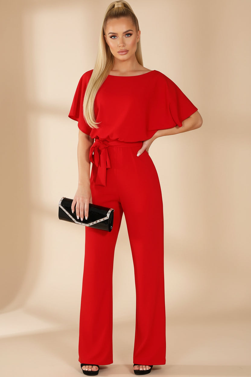 Woman wearing a red jumpsuit holding a black clutch against a white background