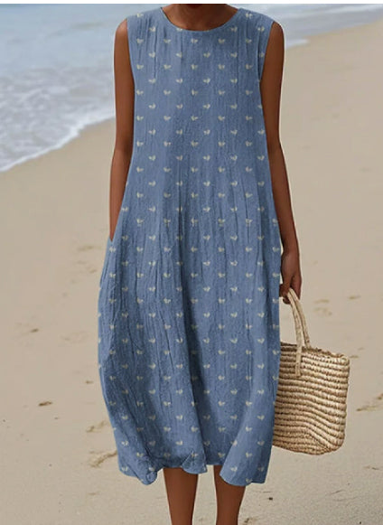 Woman in a blue dress with a subtle pattern standing on a beach.