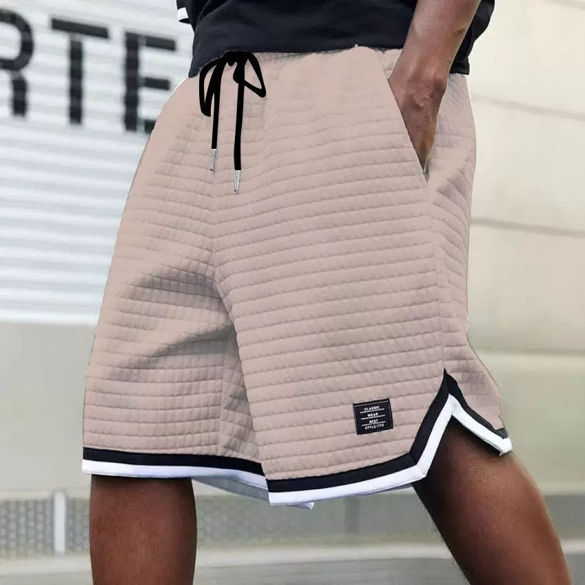 Beige quilted shorts with black and white trim worn by a person, blurred background