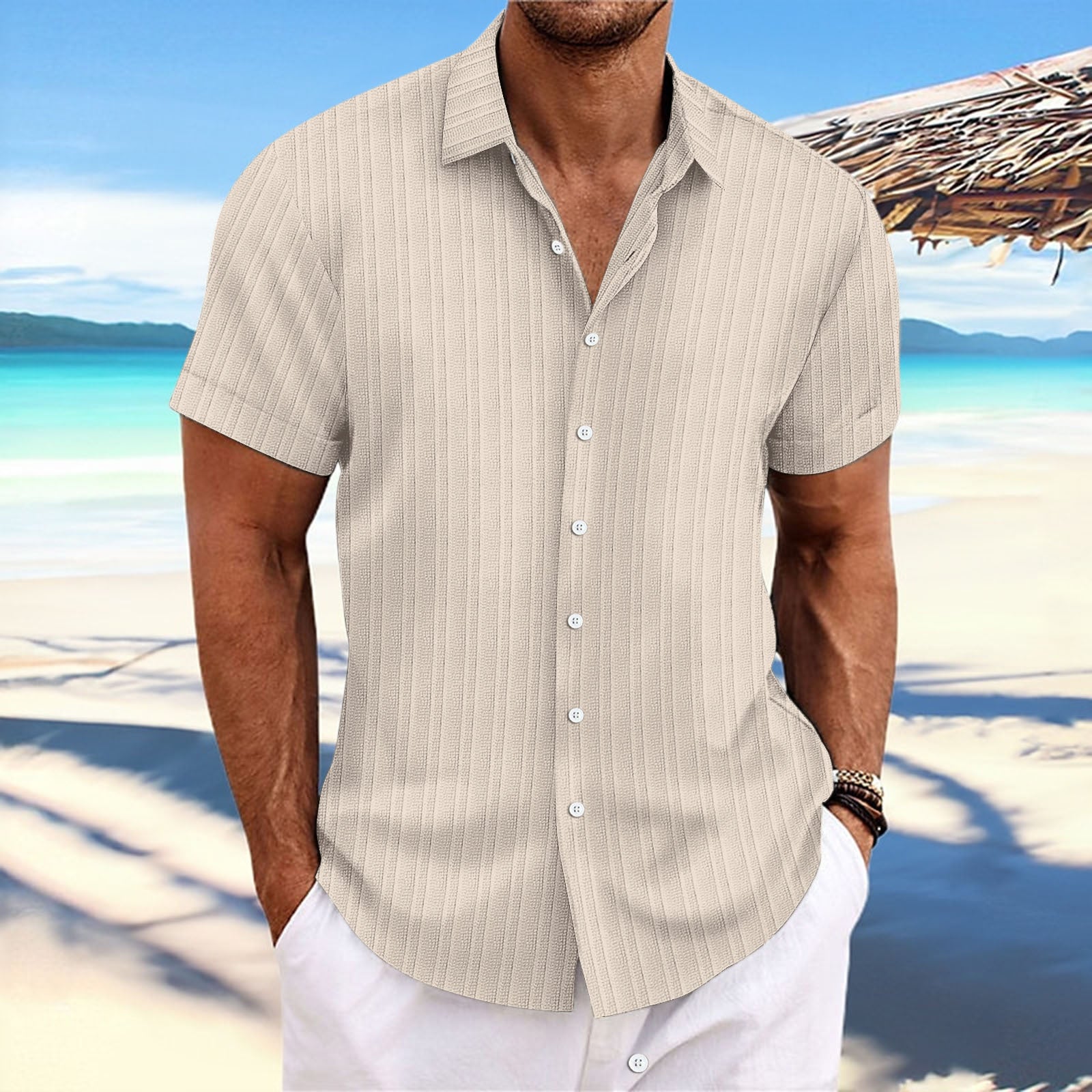 Man wearing a beige striped shirt and white pants on a beach with clear blue water and sky.