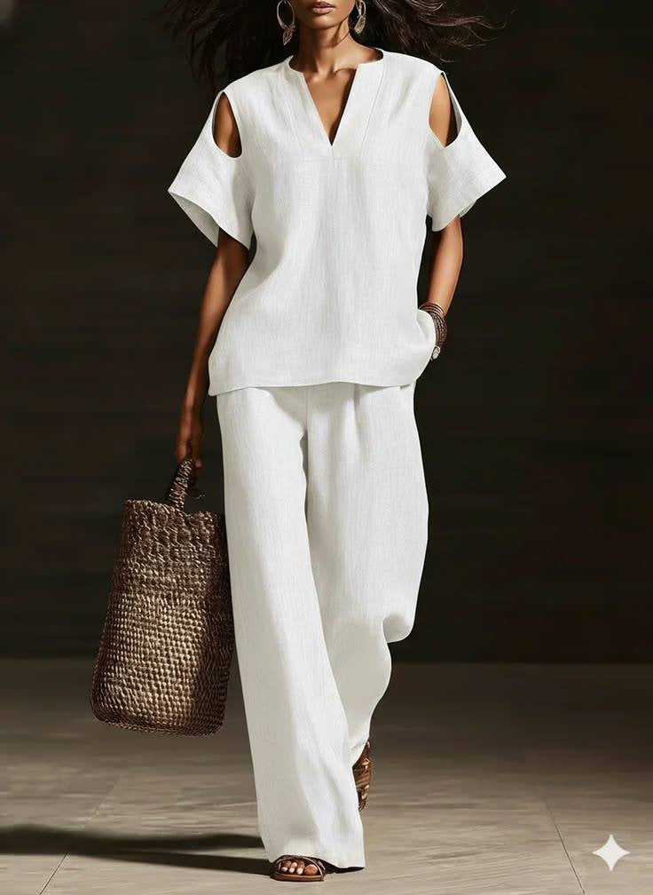 Woman wearing a white outfit with wide-leg pants and a straw bag on a dark background