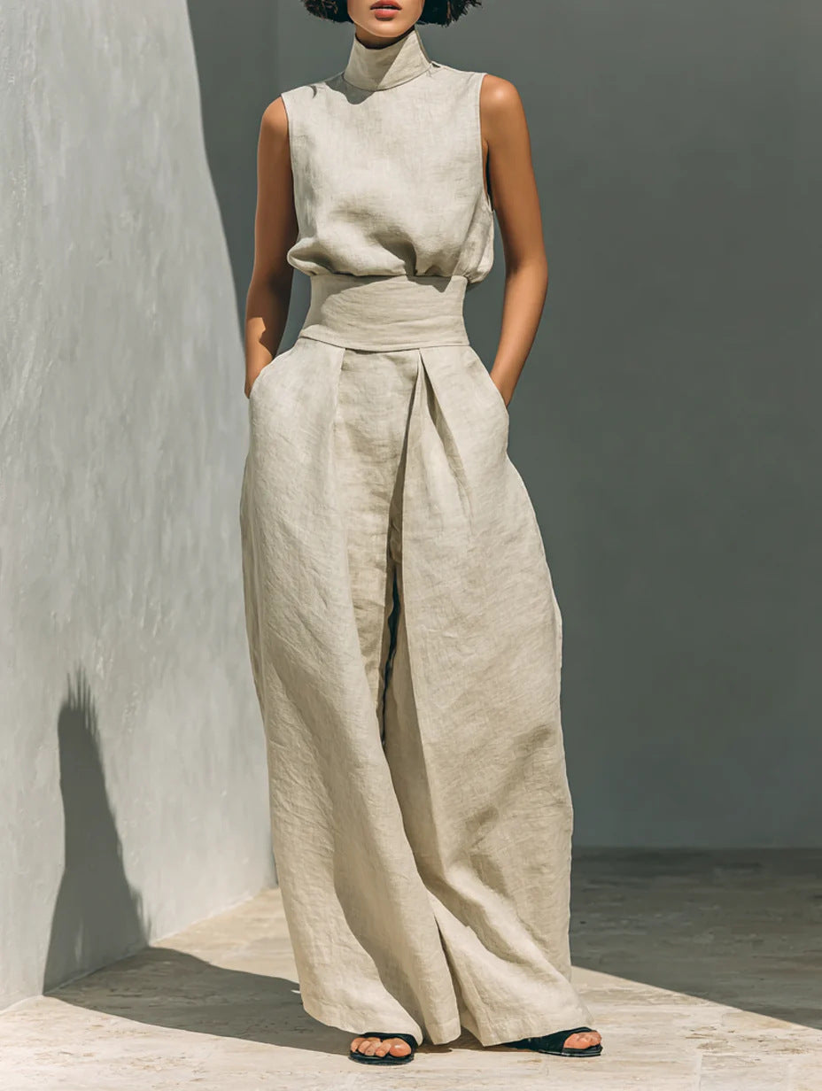 Person wearing a beige sleeveless top and wide-leg pants against a gray wall.