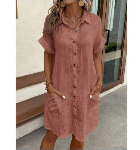 Woman wearing a pink button-up dress standing in front of a building entrance.