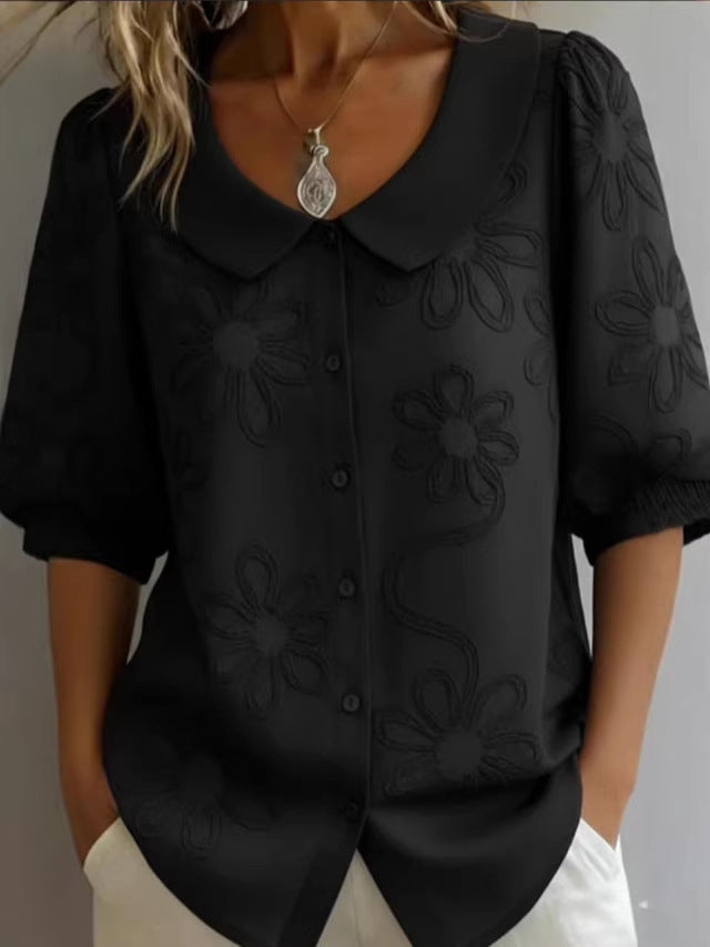 Black blouse with floral embroidery worn by a person on a neutral background