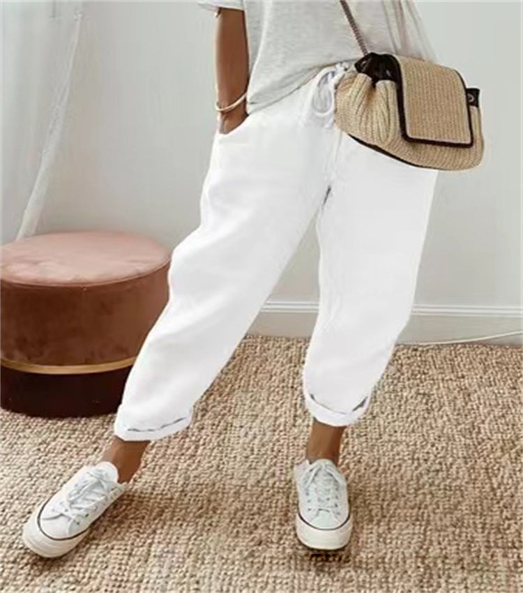 Person wearing white pants and sneakers with a beige bag, standing on a textured floor.