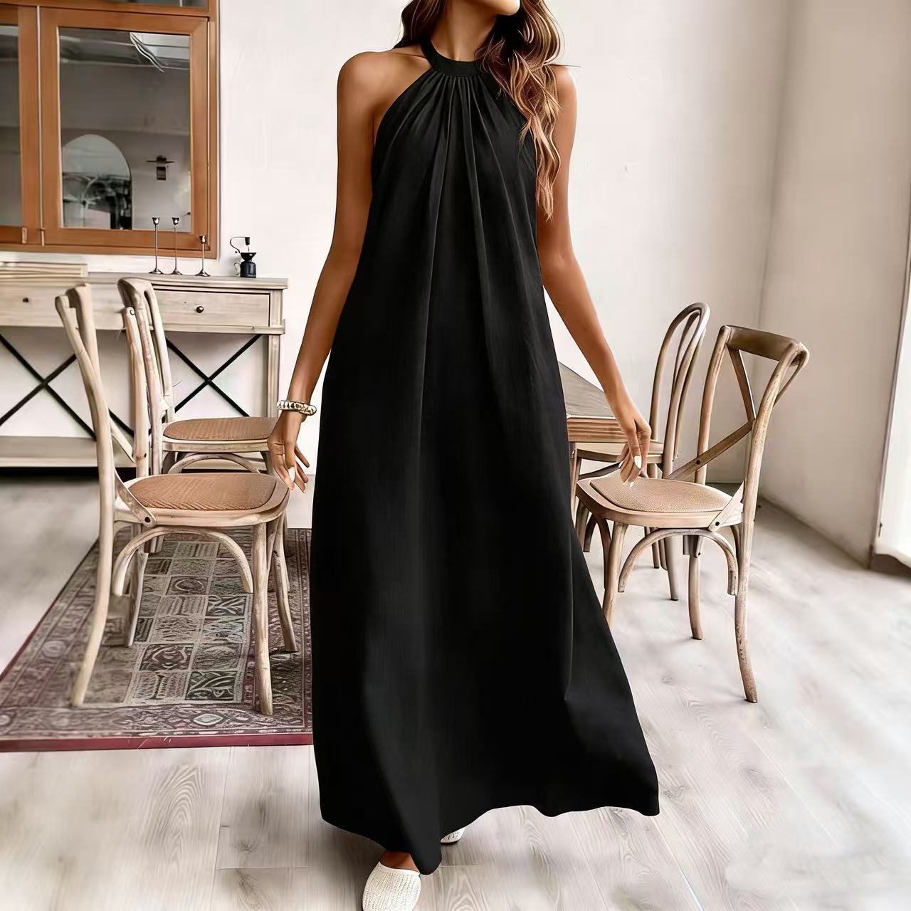 Woman wearing a black halter neck dress in a room with wooden chairs and a mirror.