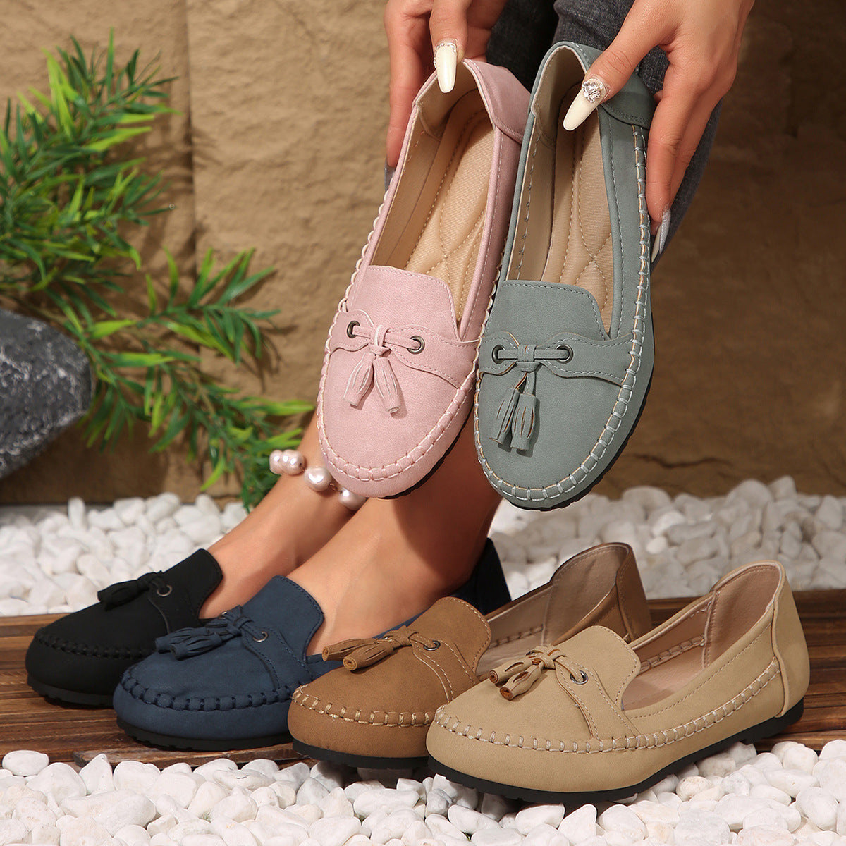 Pair of pink loafers held above a collection of various colored loafers on pebbles with a natural background.