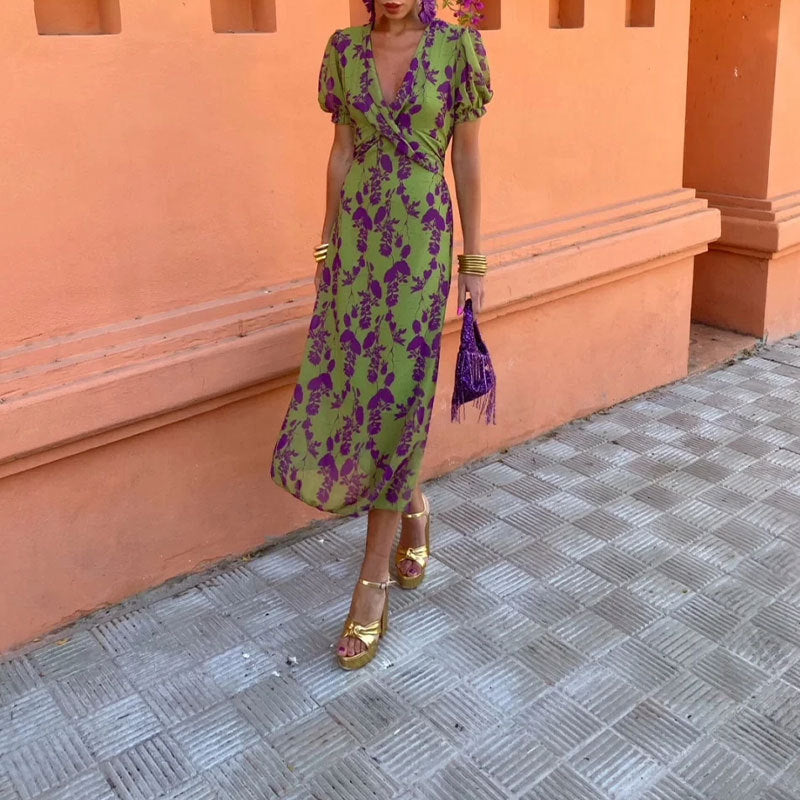 Woman in a green and purple floral dress standing against an orange wall.