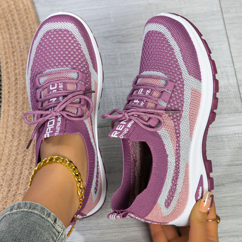 Purple running shoes with white soles worn by a person on a light gray floor.