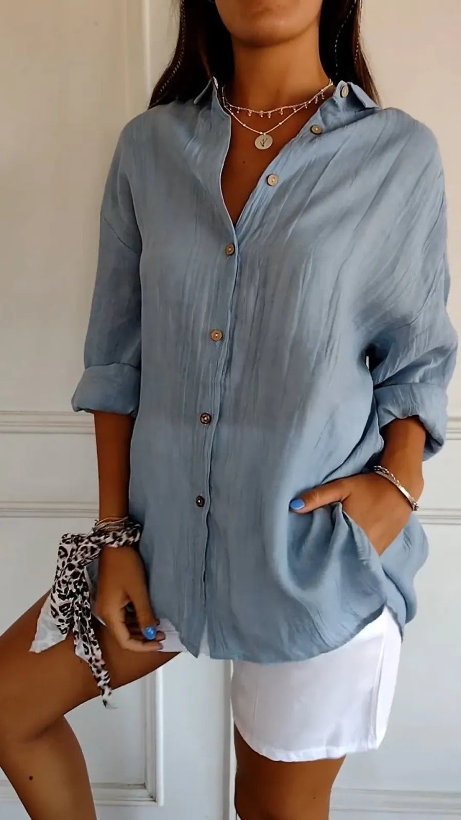 Woman wearing a light blue button-up shirt with rolled-up sleeves and white shorts.