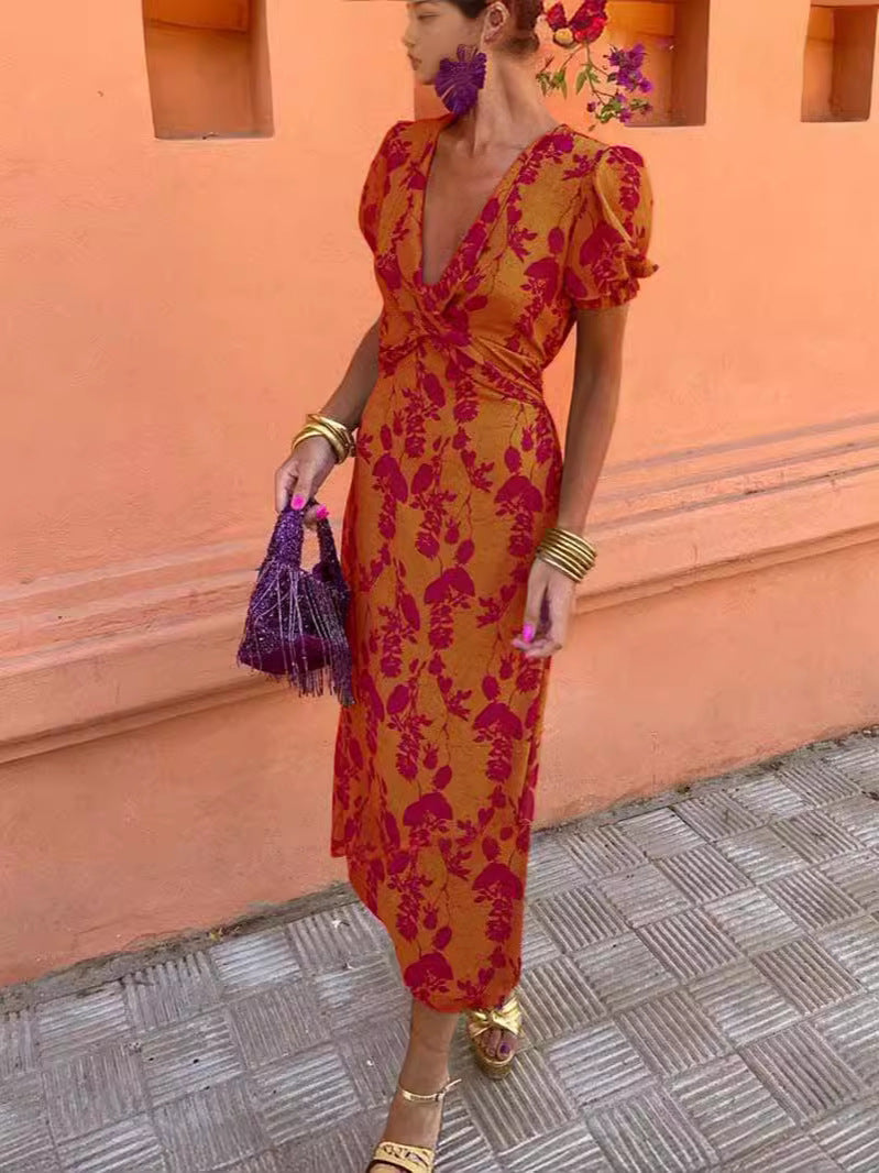 Woman in a red and orange floral dress standing against a pink wall.