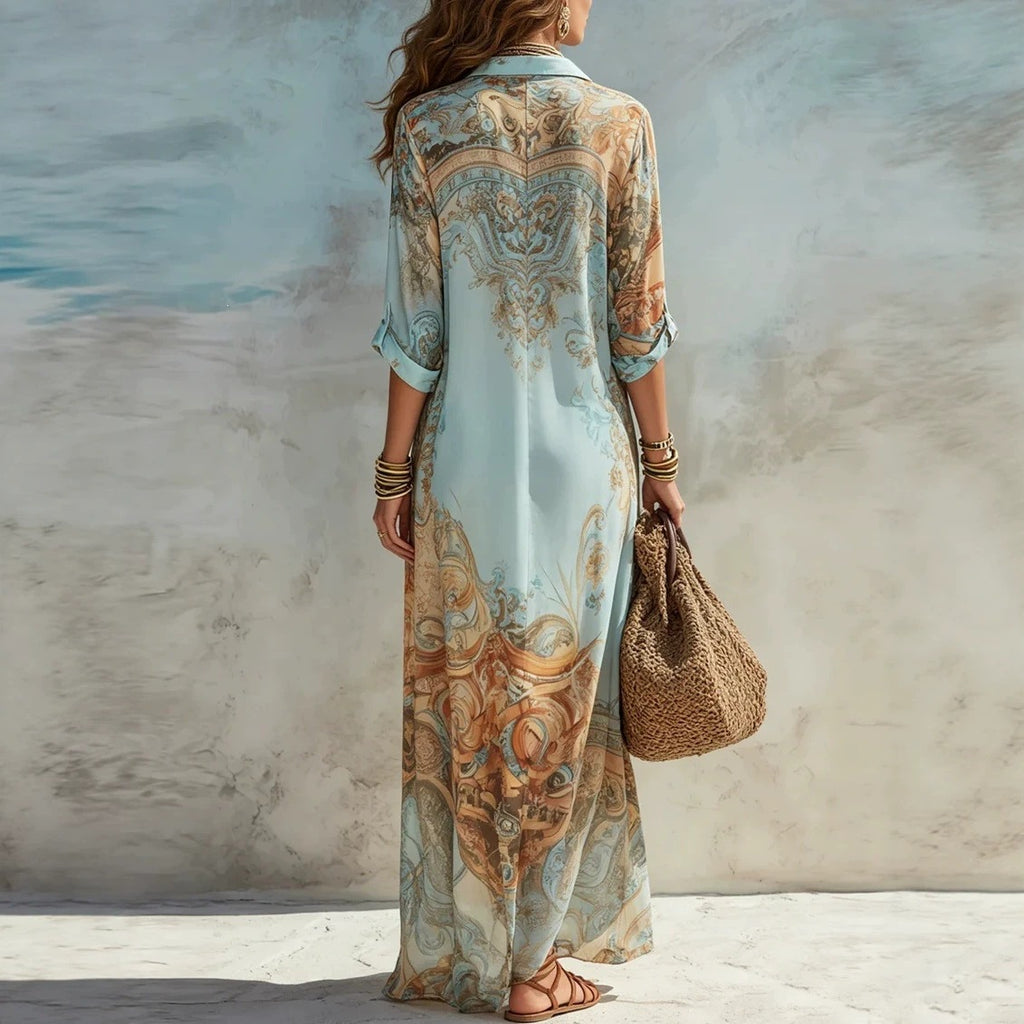 Woman wearing a long, patterned dress holding a woven bag against a textured wall.