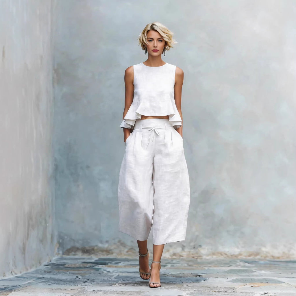Woman wearing a white sleeveless top and wide-leg pants against a textured wall.