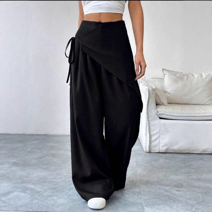 Person wearing black wide-leg pants in a minimalistic room with a white sofa.