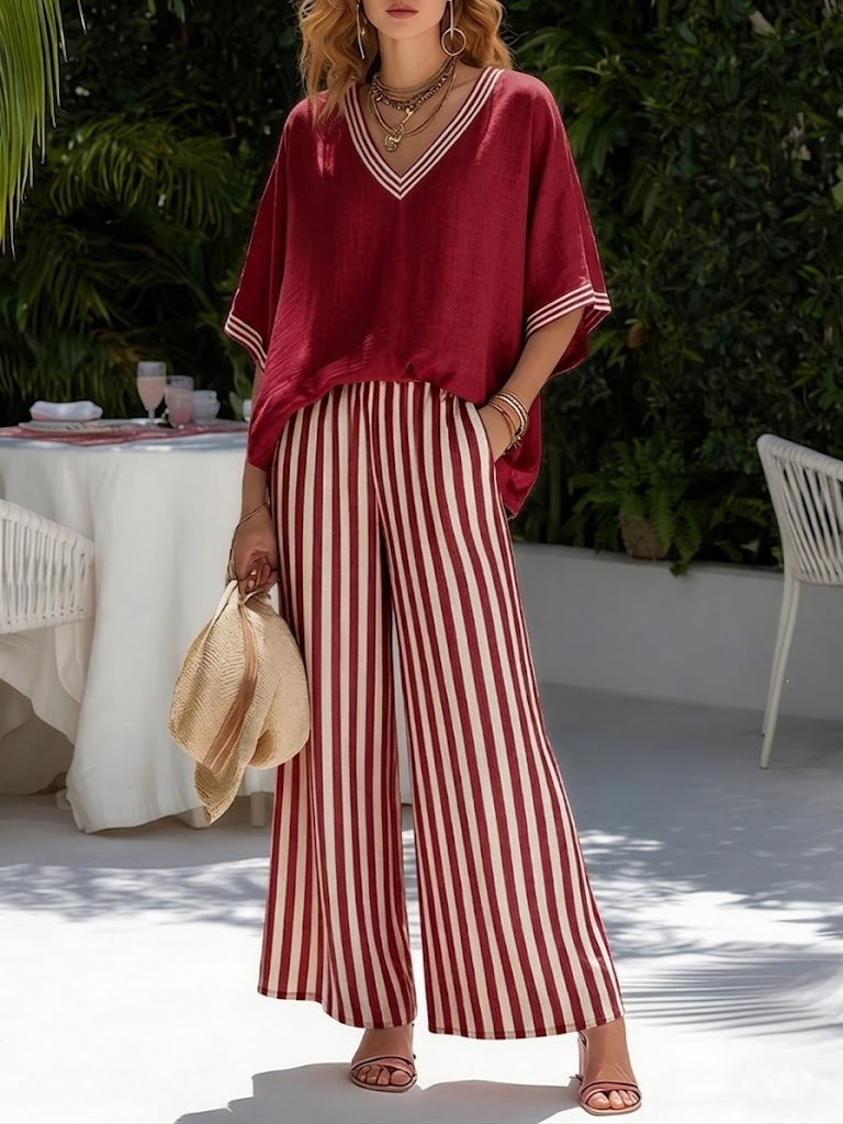 Woman wearing a red top and striped pants outdoors with a table and chairs in the background.
