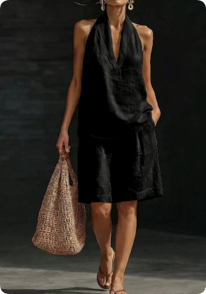 Woman in a black outfit holding a woven bag against a dark background
