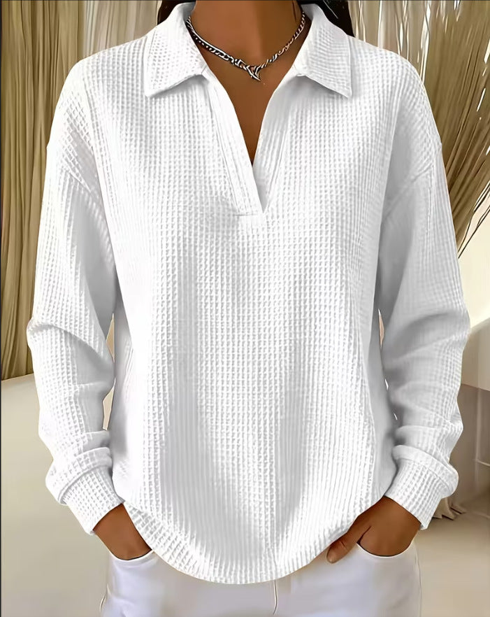 A woman wearing a white waffle-knit long-sleeve polo shirt with a collar and split button placket, paired with white pants and a silver chain necklace.