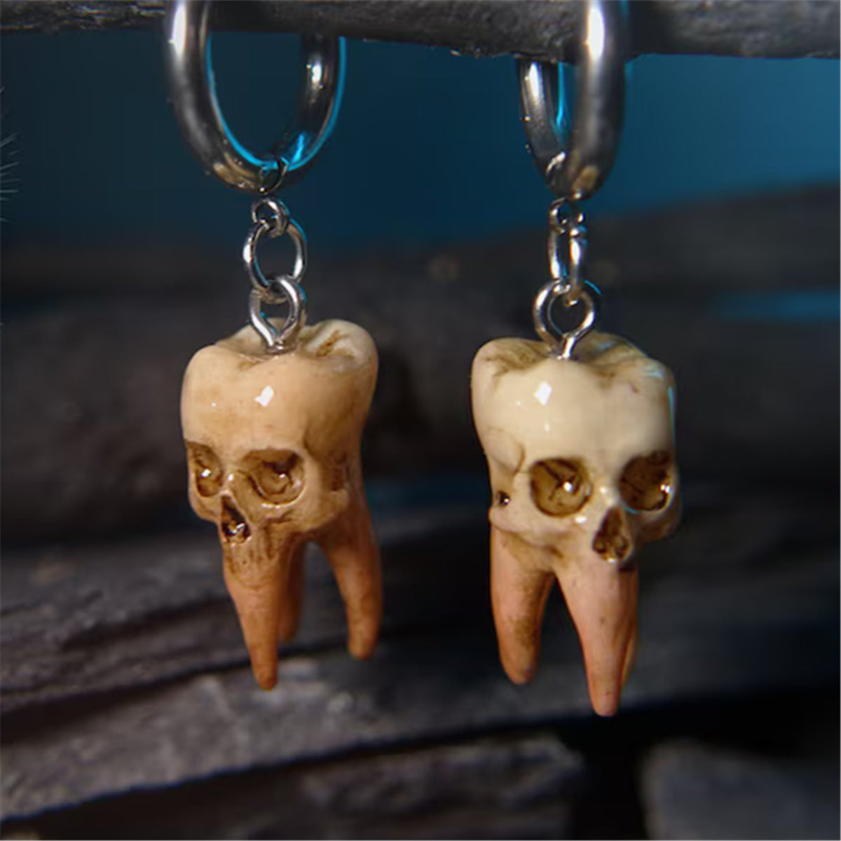 Tooth-shaped earrings with skull designs hanging from a dark surface.