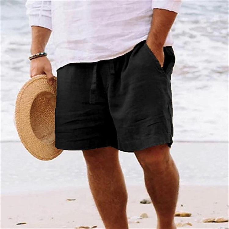 Person wearing black shorts and holding a straw hat on a beach.