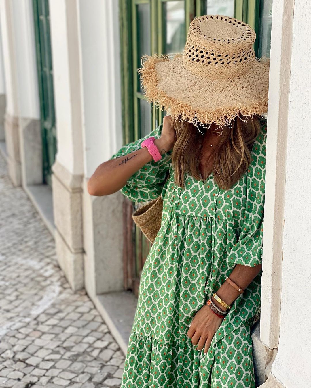 Person wearing a green patterned dress and straw hat on a gray background