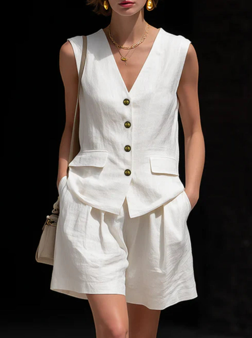 Person wearing a white sleeveless top and shorts set with gold buttons on a black background