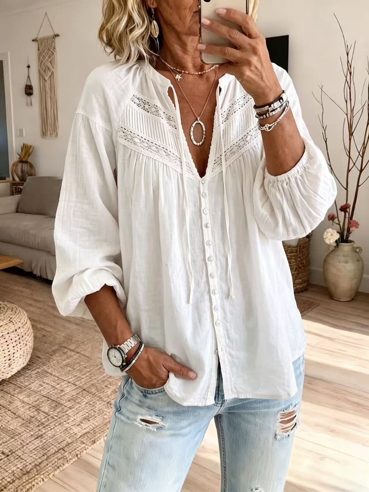 A woman takes a mirror selfie wearing a white long-sleeve button-up blouse with delicate lace embroidery across the chest, paired with light-wash distressed jeans.