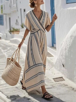 Woman in a long, patterned dress walking on a sunlit street with white buildings.