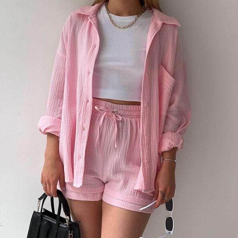 Woman wearing pink loungewear set and white crop top, styled with gold necklace, black handbag