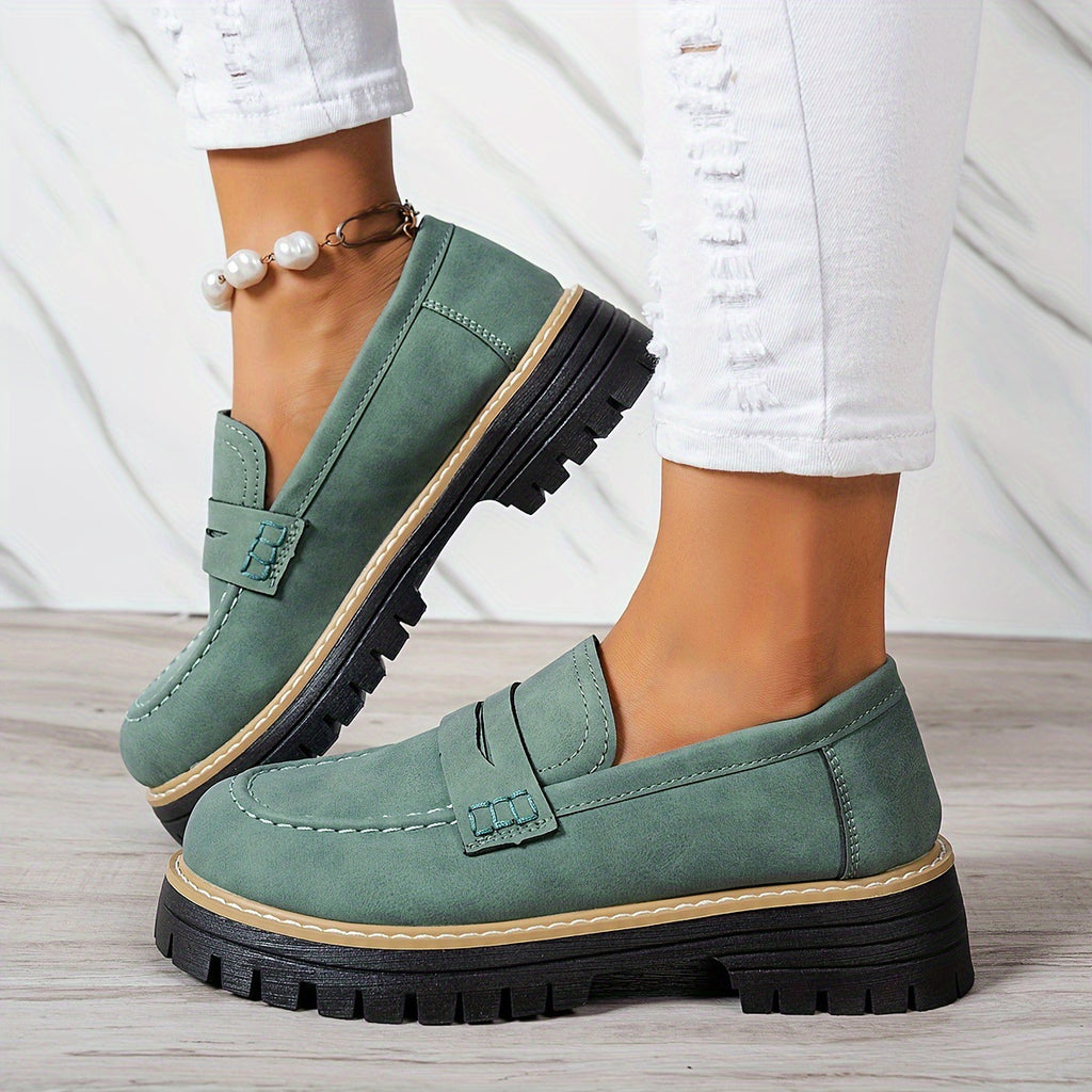 Green loafers worn with white pants on a light wooden floor.