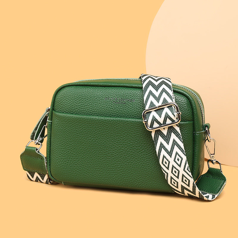 Green handbag with a patterned strap on a beige background