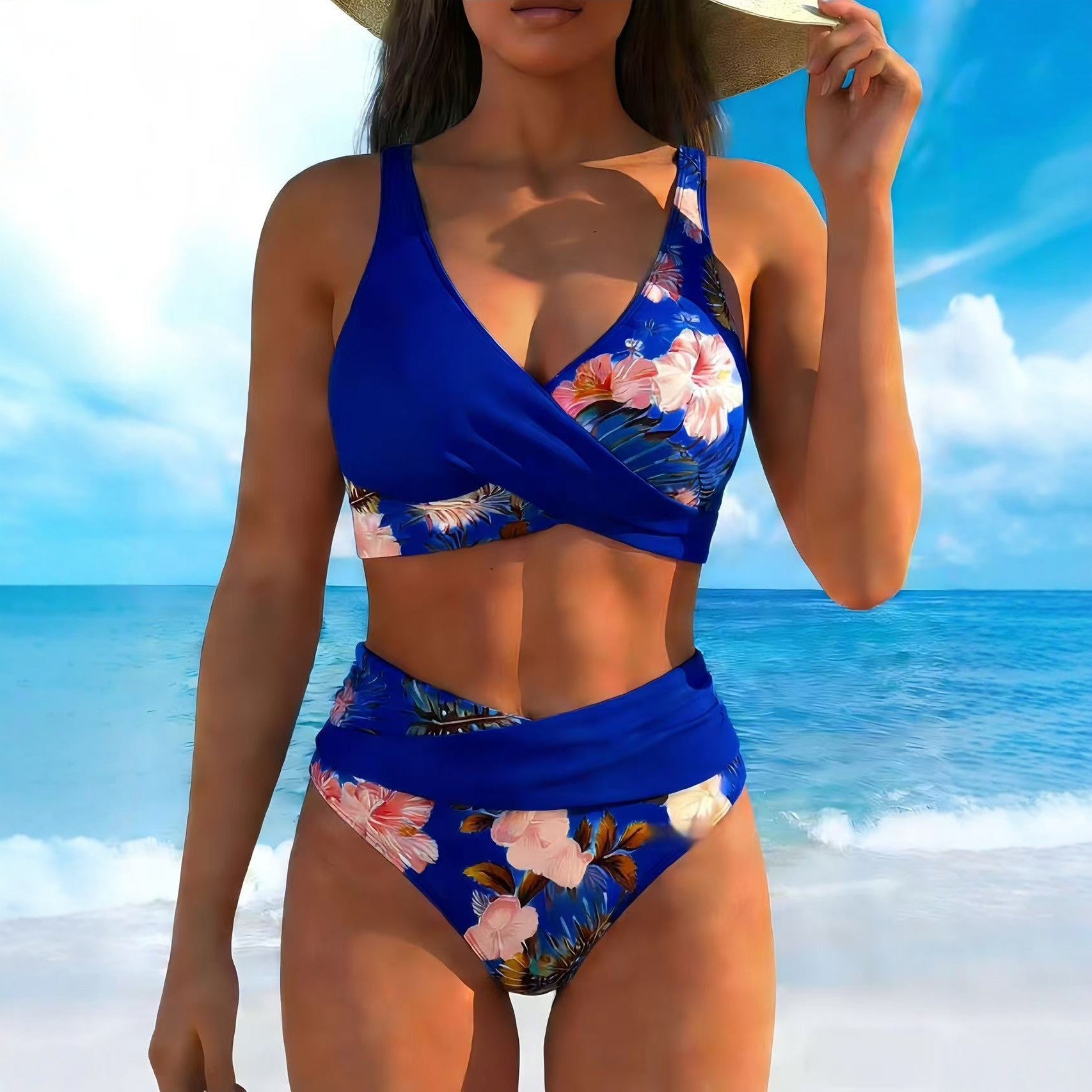 Woman wearing a blue floral bikini set on a beach with clear blue sky and ocean.