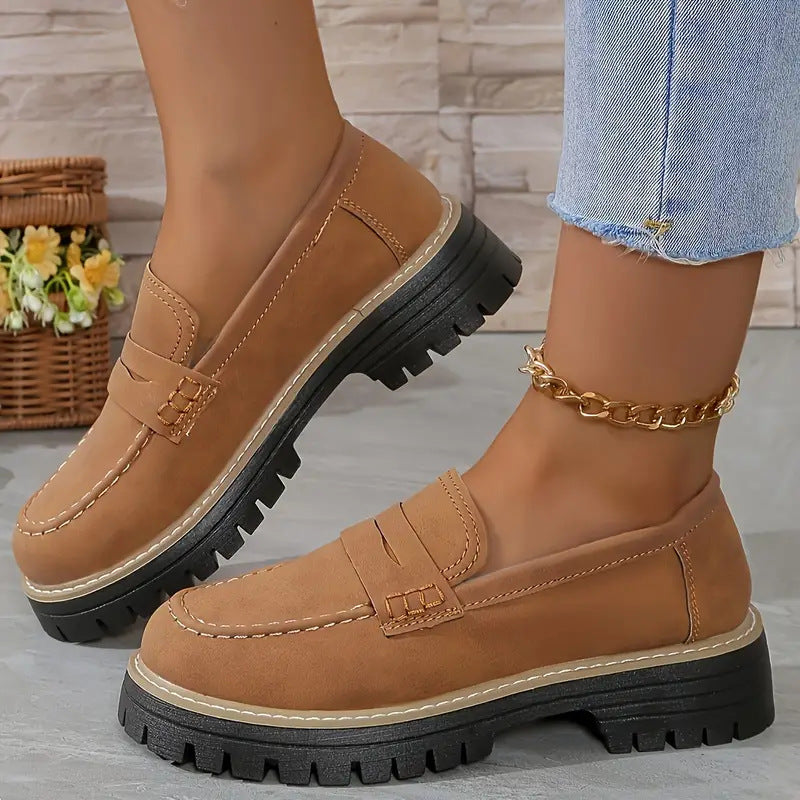 Brown loafers with black soles worn by a person on a neutral background