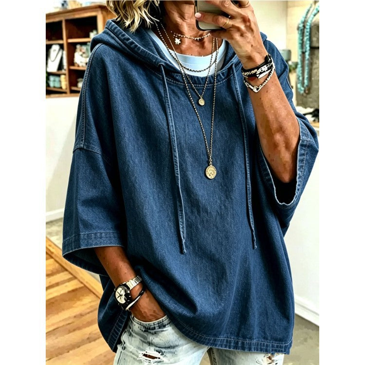 A woman takes a mirror selfie wearing an oversized dark blue denim hooded sweatshirt with wide three-quarter sleeves, layered over a light blue t-shirt and paired with distressed light-wash jeans.
