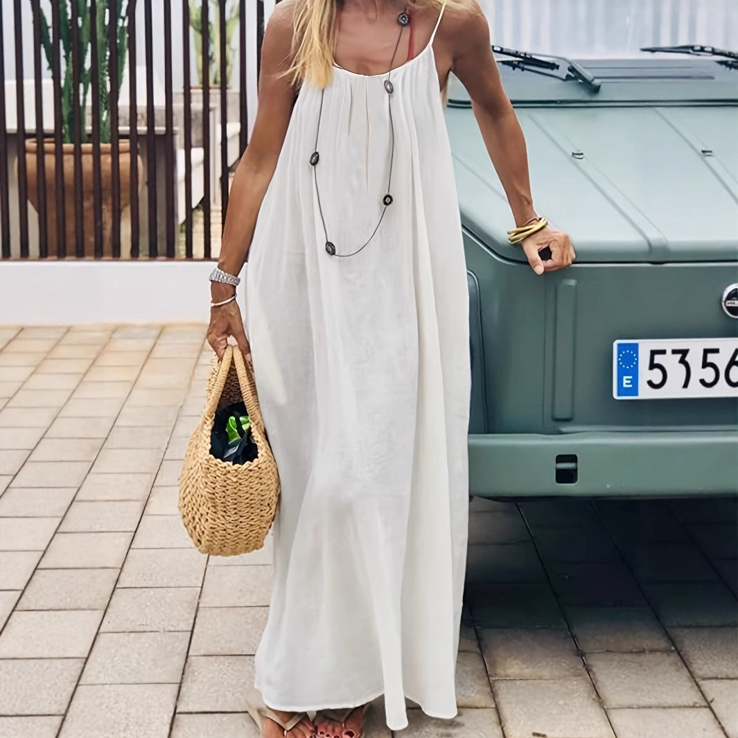 Woman in a long white dress holding a woven bag, standing next to a green car.
