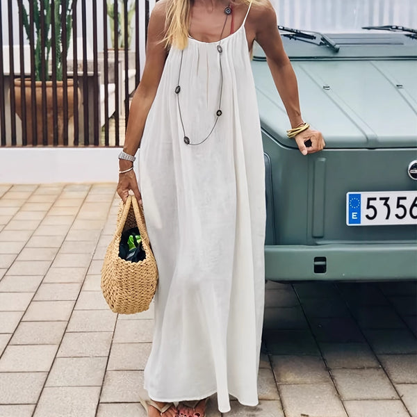 Woman in a long white dress holding a woven bag, standing next to a green car.