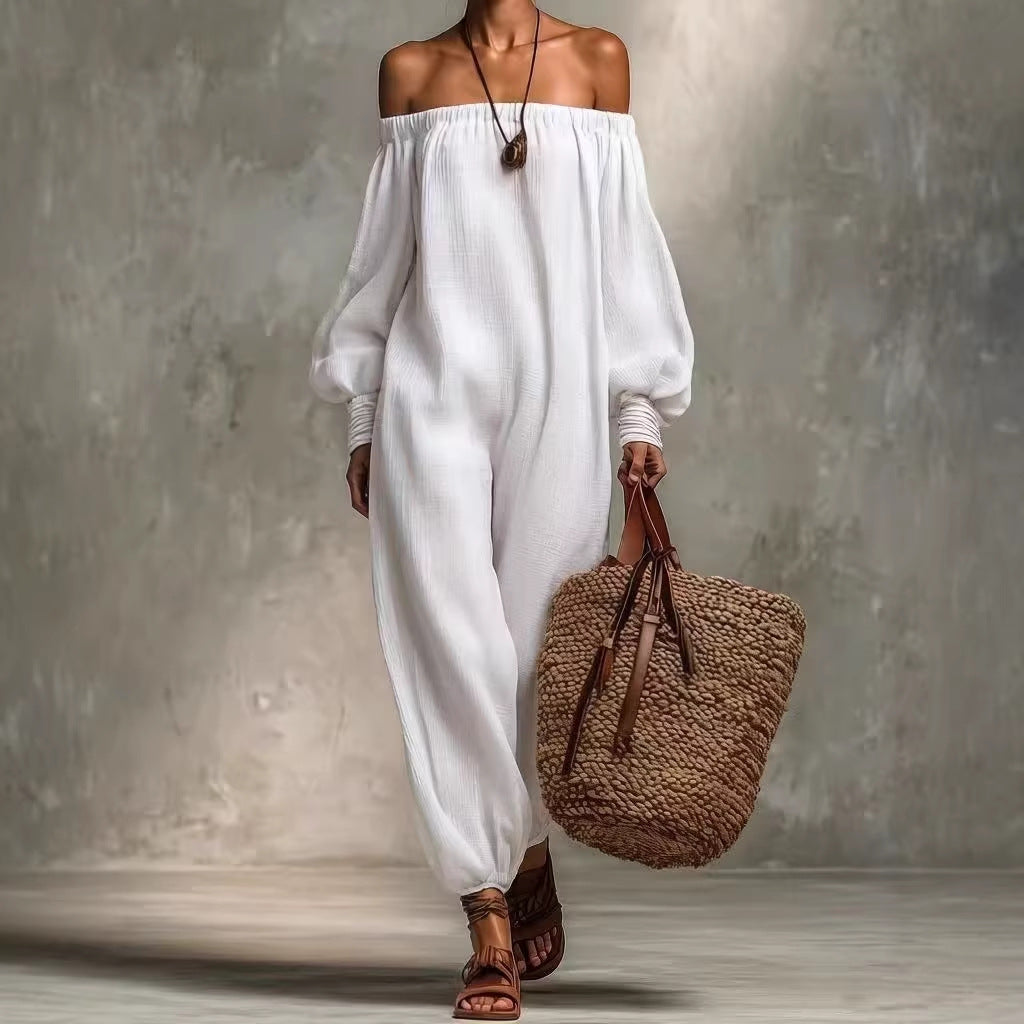 Person wearing a white off-shoulder top and white pants, holding a woven brown bag against a gray background.