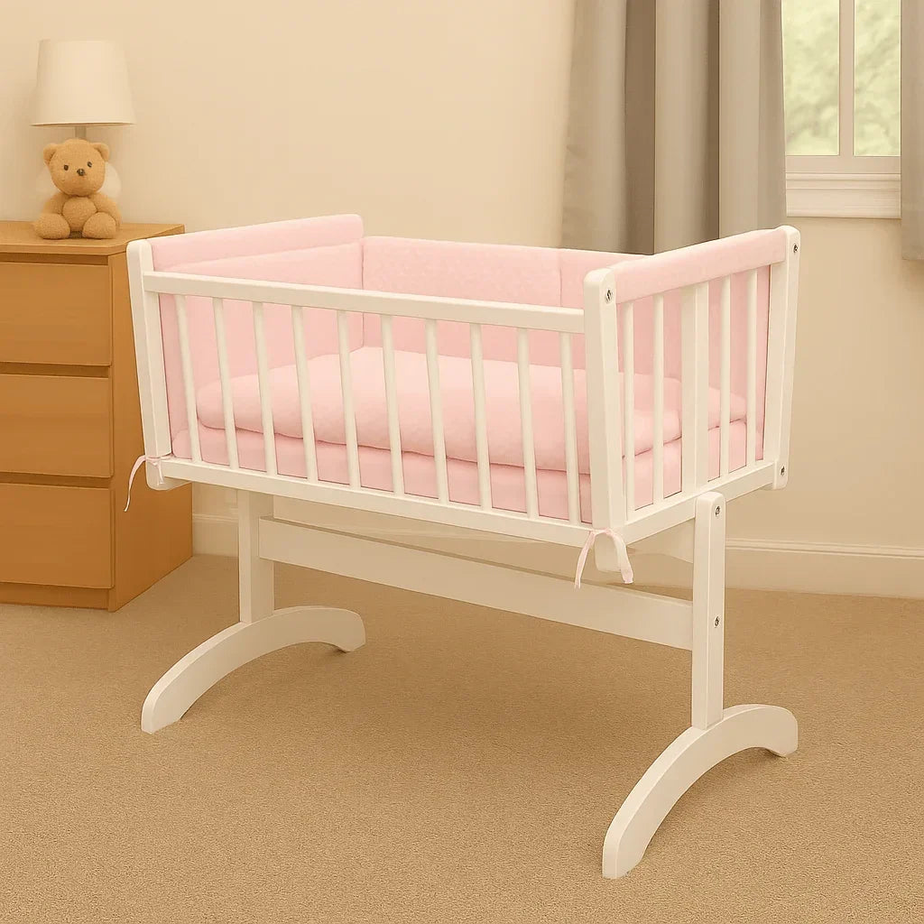 White wooden cradle with soft pink quilt and bumper bedding set in a cozy nursery room