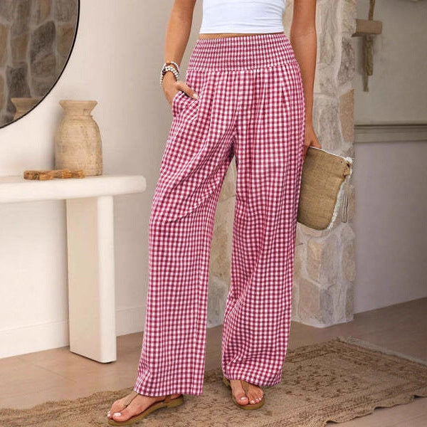 Person wearing pink checkered pants standing in a room with a stone wall and white pedestal table.
