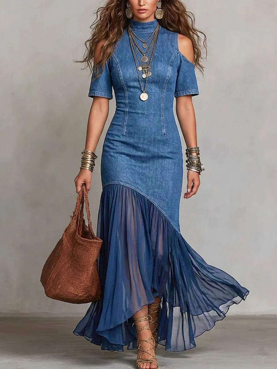 Woman wearing a blue denim dress with sheer overlay holding a brown handbag against a plain background