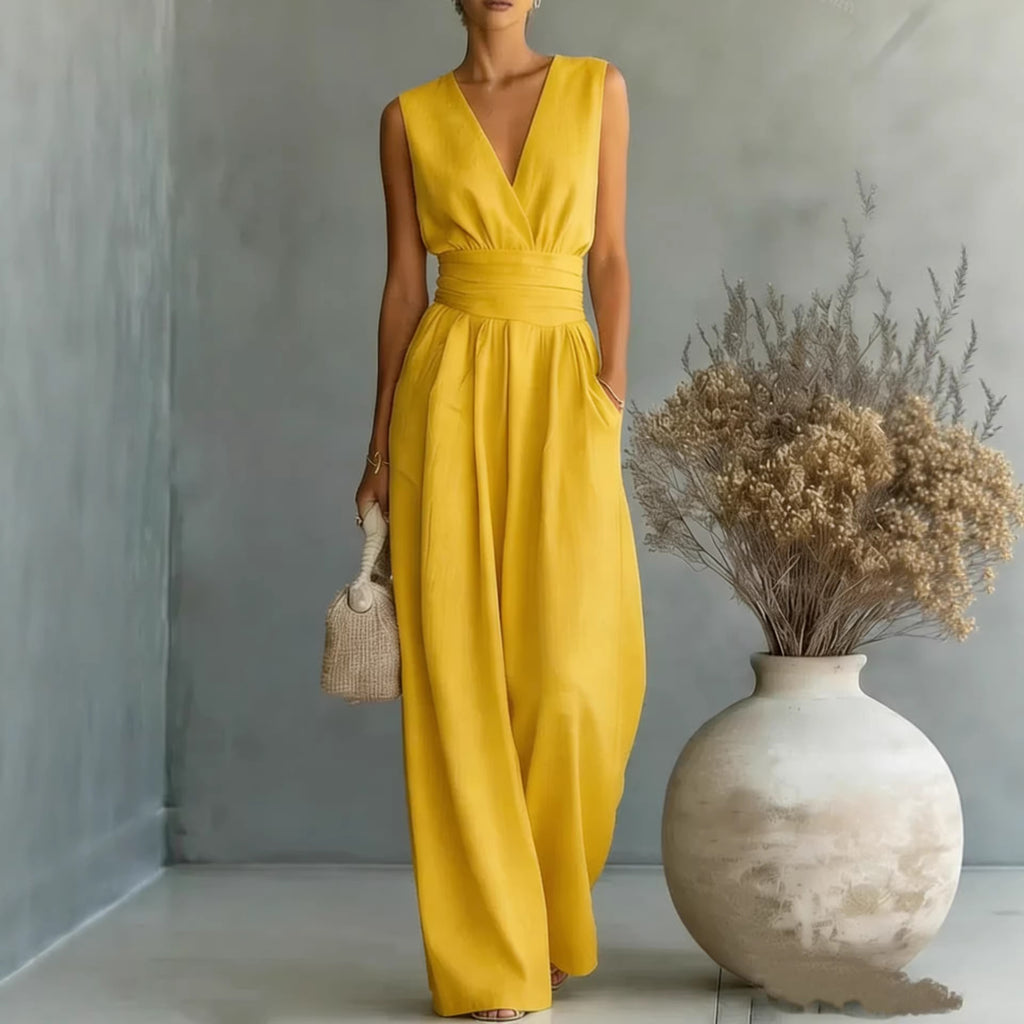 Woman in a yellow dress standing next to a vase with dried flowers indoors.
